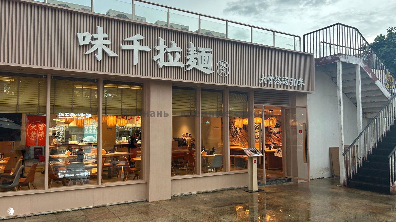 Фасад AJISEN RAMEN в бухте Ялонг с вывеской на китайском, большими окнами и видом на почти пустые столики внутри.