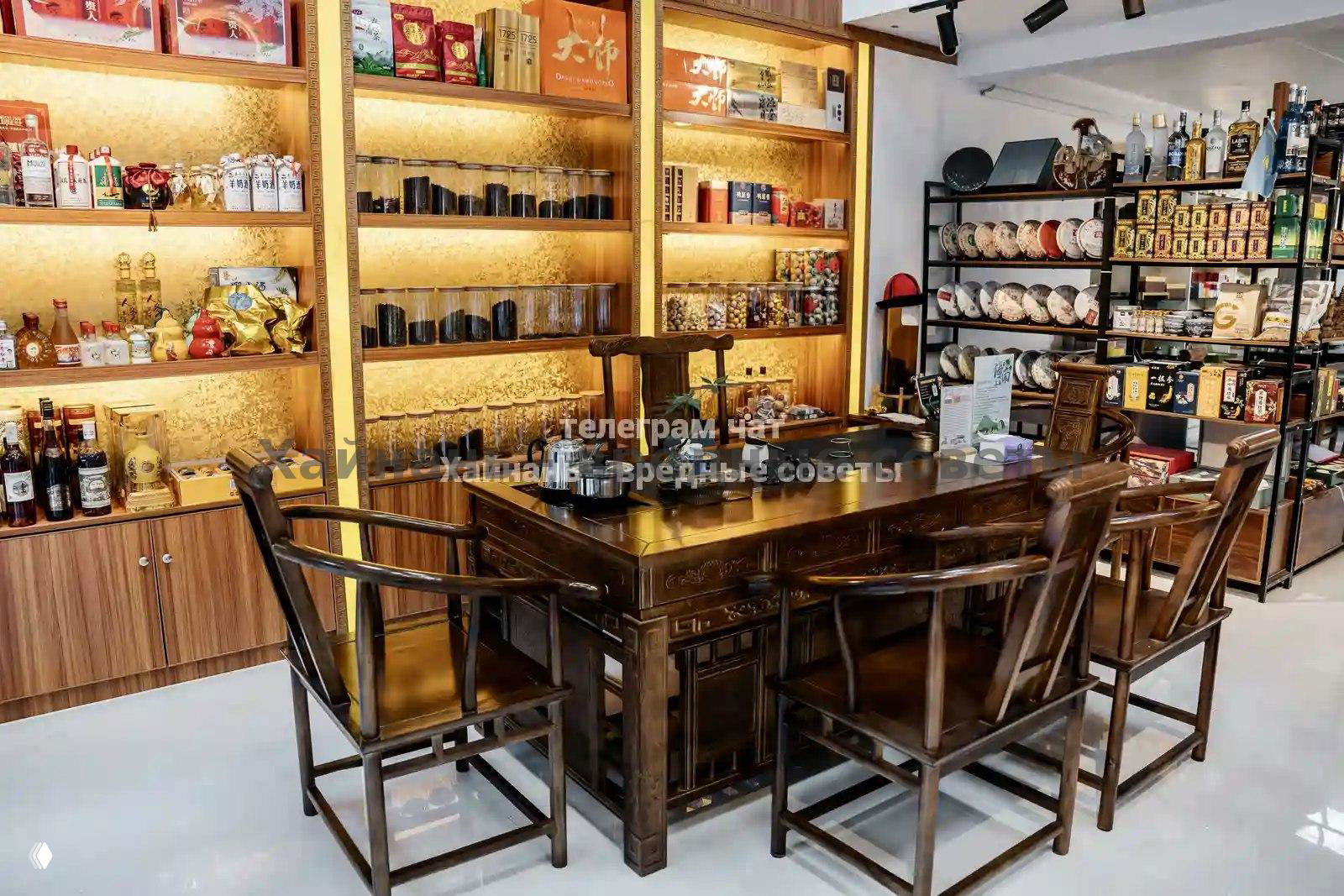 Внутренний вид магазина с чайным столом и деревянной мебелью: полки с упаковками чая, сувенирами и подарками на заднем фоне.