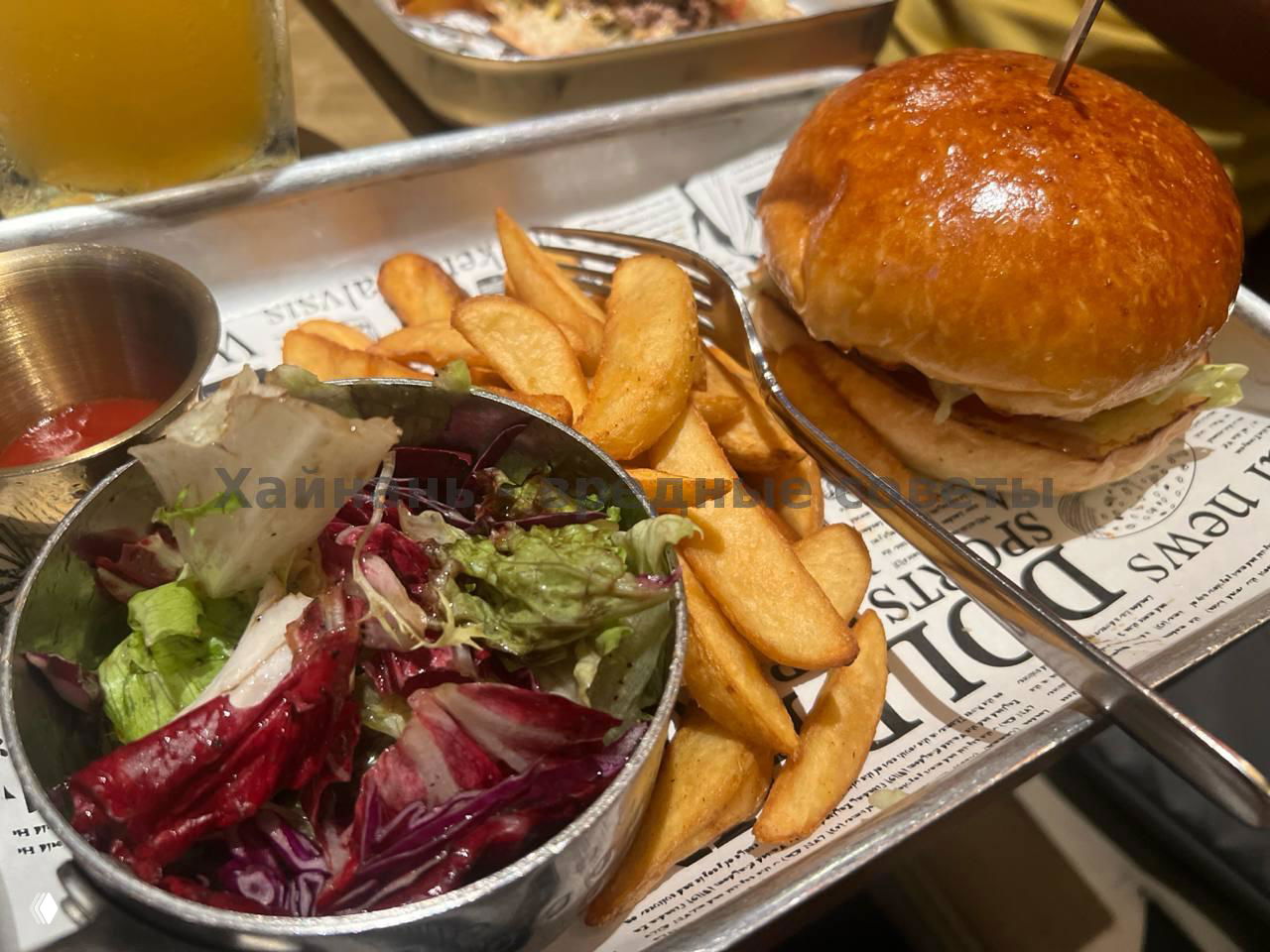 Бургер с картофелем-дольками и миской салата на металлическом подносе в баре «Дельфин», крупный план блюда и сервировки на столе.