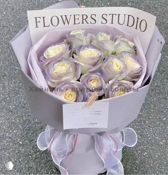 Крупный букет светло-сиреневых и кремовых роз в круглой фирменной упаковке с карточкой и бантом, фото сверху на фоне серого пола, демонстрация сервиса.