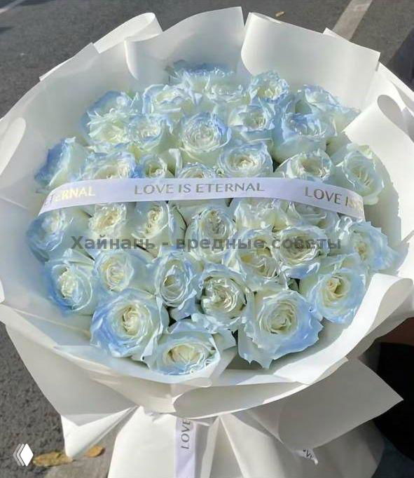 Большой монобукет белых роз с лёгким голубоватым оттенком, оформлен в белую матовую бумагу с лентой «LOVE IS ETERNAL», фото подчёркивает объём и текстуру цветов.