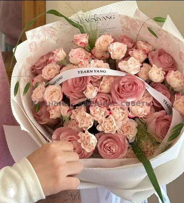 Круглый букет пудрово-розовых кустовых роз в цилиндрической шляпной коробке с брендовой лентой, аккуратно оформленный, фото показывает боковой ракурс композиции.