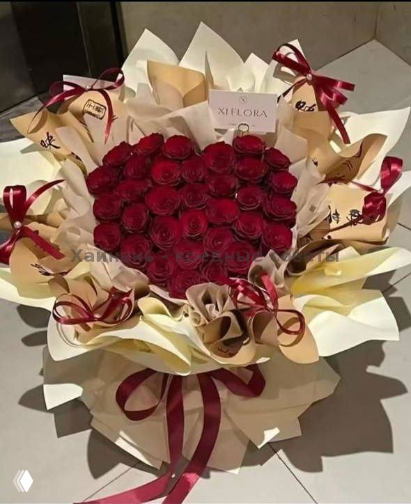 Большая композиция из тёмно-красных роз, сложенная в форме сердца с декоративными бантиками и золотистой упаковкой, эффектный подарок для торжеств и сюрпризов.