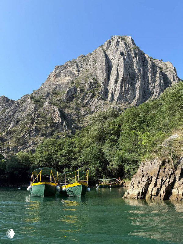 Две желто-зелёные лодки на спокойной изумрудной воде у подножия высокой скалистой стены каньона в резервате.