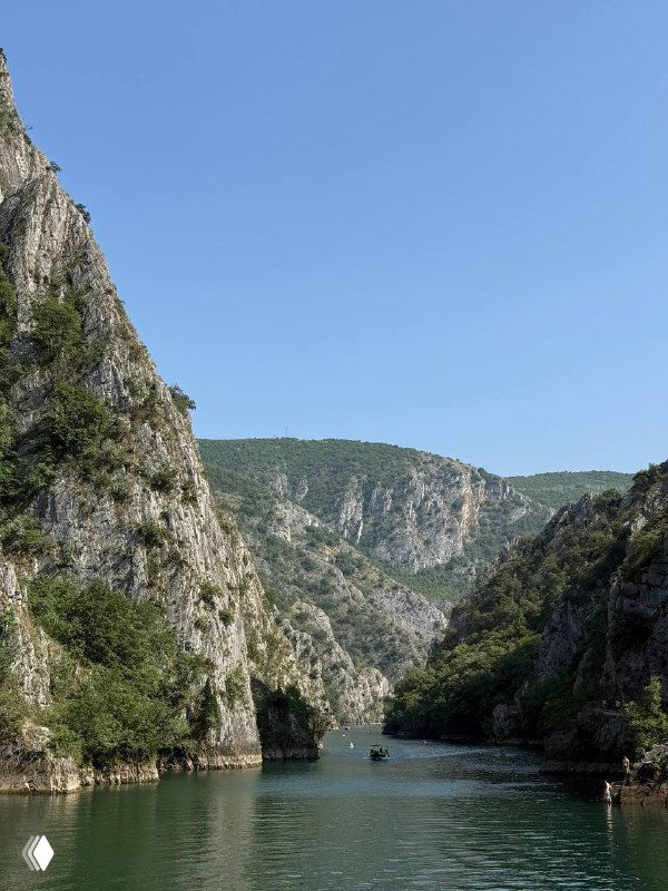 Широкий вид на узкий речной каньон с отвесными скалами и медленно текущей зелёной водой, лодки вдалеке.