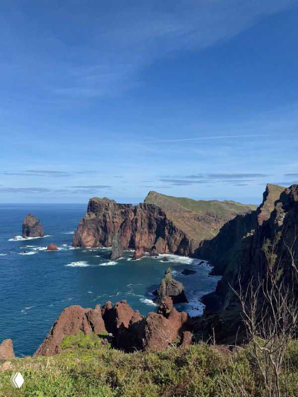 Океанский берег с крупными красно-коричневыми скалами и прибоями под ясным голубым небом — пейзаж из поездки, акцент на природе и рельефе.