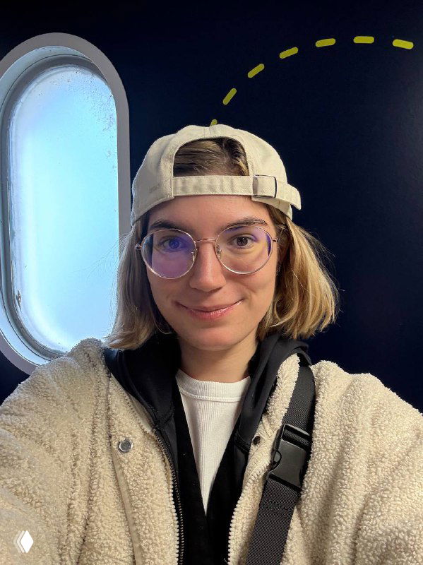 Портрет автора в кепке и очках у иллюминатора самолёта: улыбка на лице, интерьер салона и окно с дневным светом на фоне.