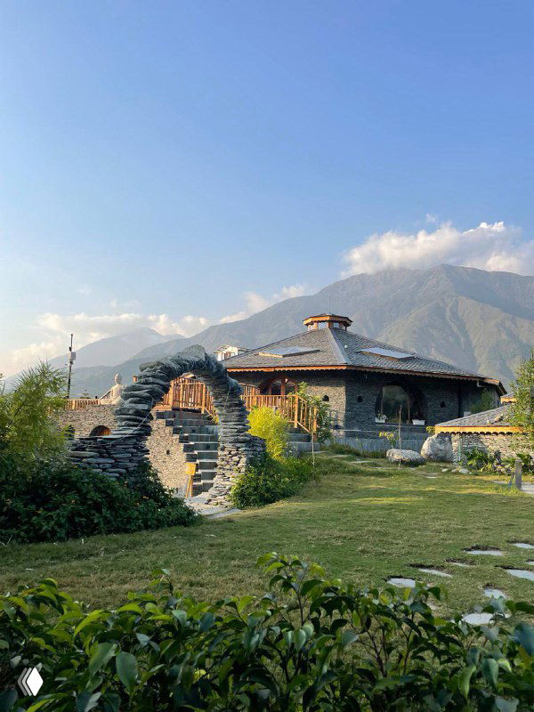 Каменные постройки и арочные проходы у подножия гор: вид на эко-отель или традиционную постройку в горной долине на фоне зелени.