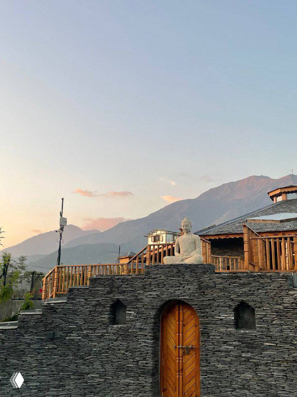 Деревянные террасы и домики на склоне гор при мягком закатном свете, силуэт гор на горизонте и спокойная атмосфера.