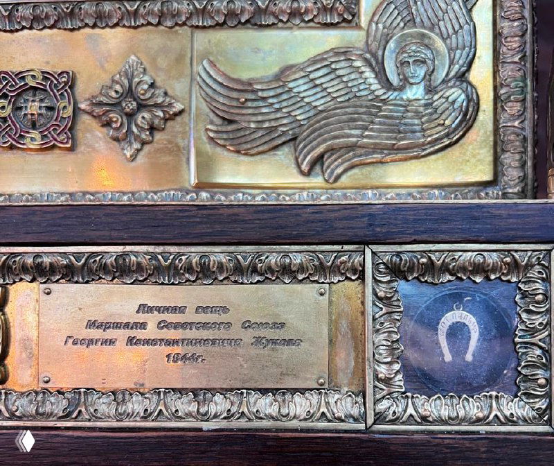 Крупный план панели иконы в Главном Храме Вооружённых сил: золотая рамка, табличка с именем Жукова и маленькая подкова.