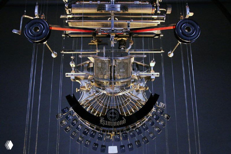 Механическая композиция из металлических элементов печатной машинки или клавиатурного механизма: ряды клавиш и рычагов висят на нитях, формируя симметрию и ритм.