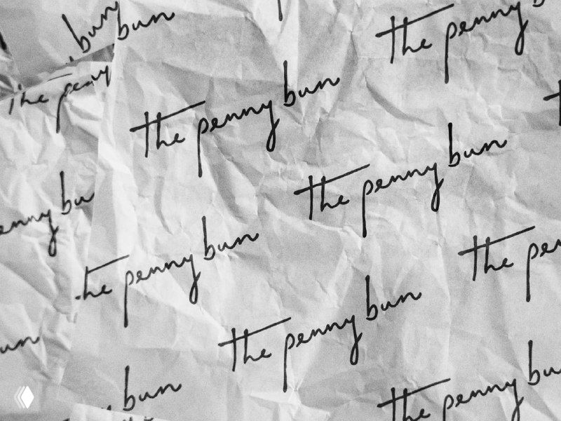 Фоновая текстура мятых листов с повторяющимся рукописным логотипом «the penny bun», образец паттерна для бренда.