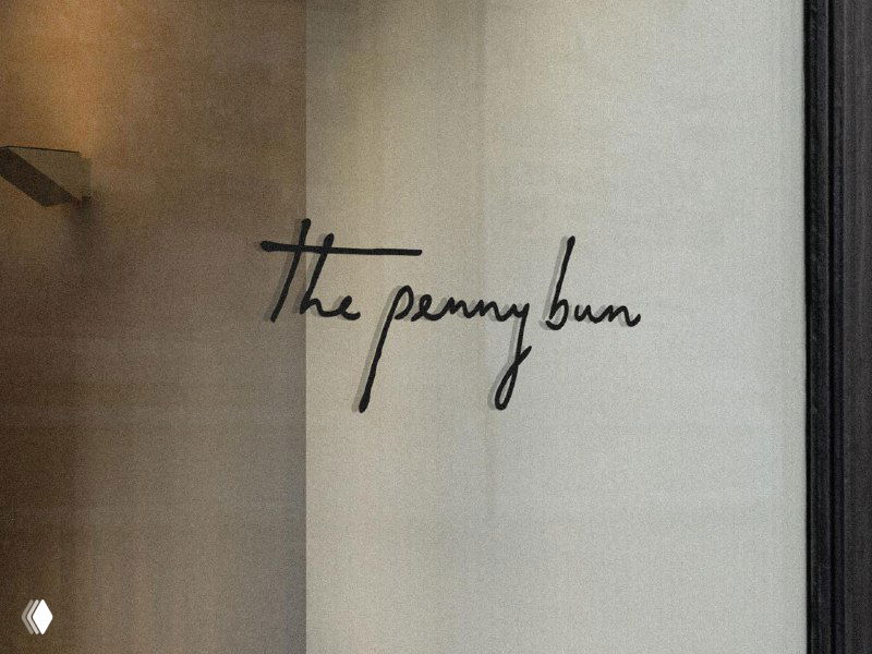 Рукописный логотип «the penny bun» на стекле витрины, демонстрация визуального применения айдентики в фасаде заведения.