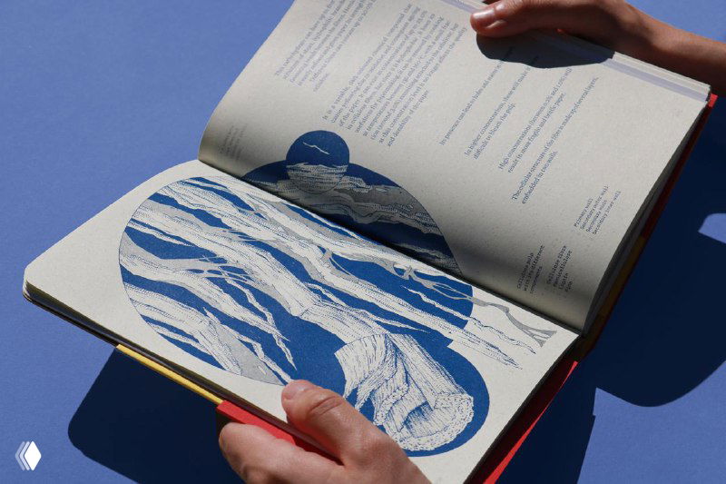 Руки держат открытую книгу с иллюстрацией синей мраморной формы; видна фактура бумаги, детализация печати и взаимодействие макета с материалом