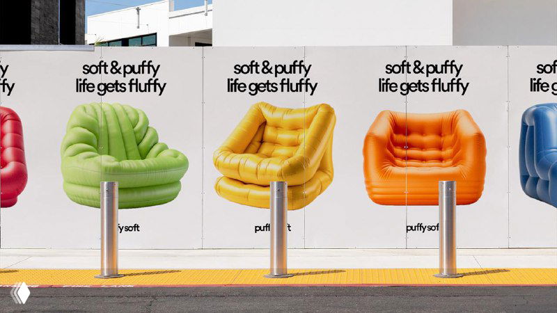 Рекламный мурал с визуализациями бренда PuffySoft: ряд постеров с яркими надувными креслами разных цветов и слоганом на городской стене.