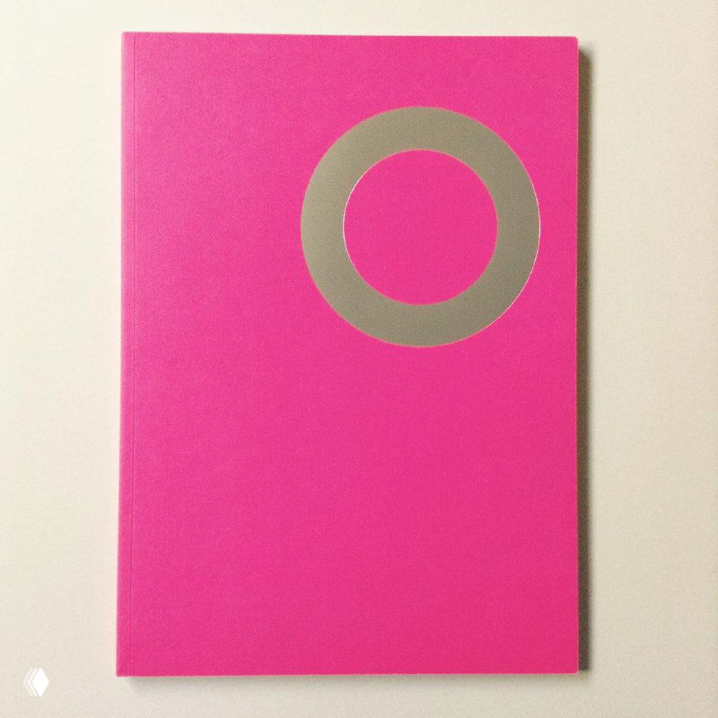 Изображение ярко-розовой обложки с крупным серебристым круговым элементом, минималистский дизайн и чистое белое окружение книги.