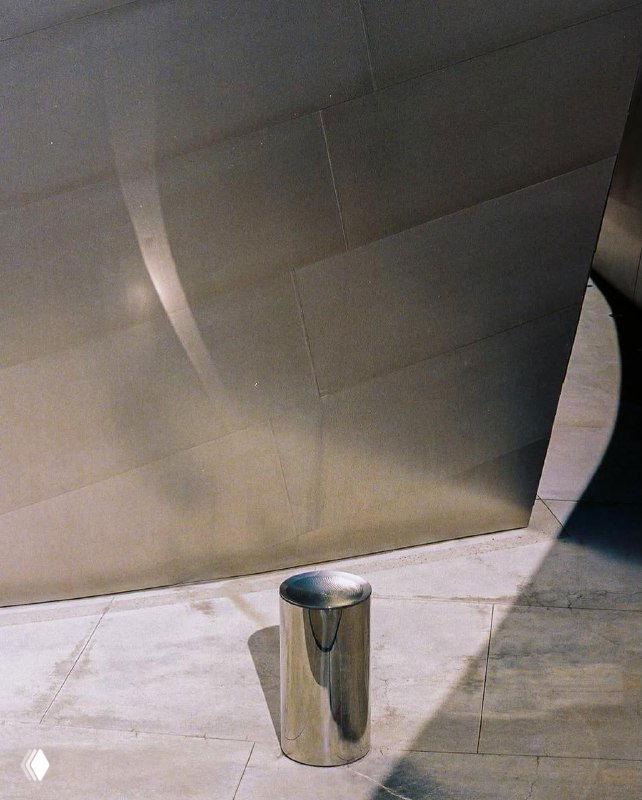 Металлический цилиндр у стены в кадре — деталь инсталляции Лахлана Турчана, где свет создаёт блики и отражения на бетонной поверхности.