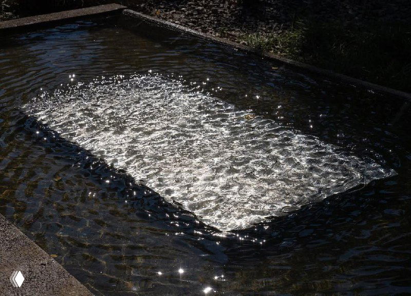 Пруд с движением воды, поверхность которого мерцает от рассеянного света — фрагмент водной световой инсталляции Лахлана Турчана.