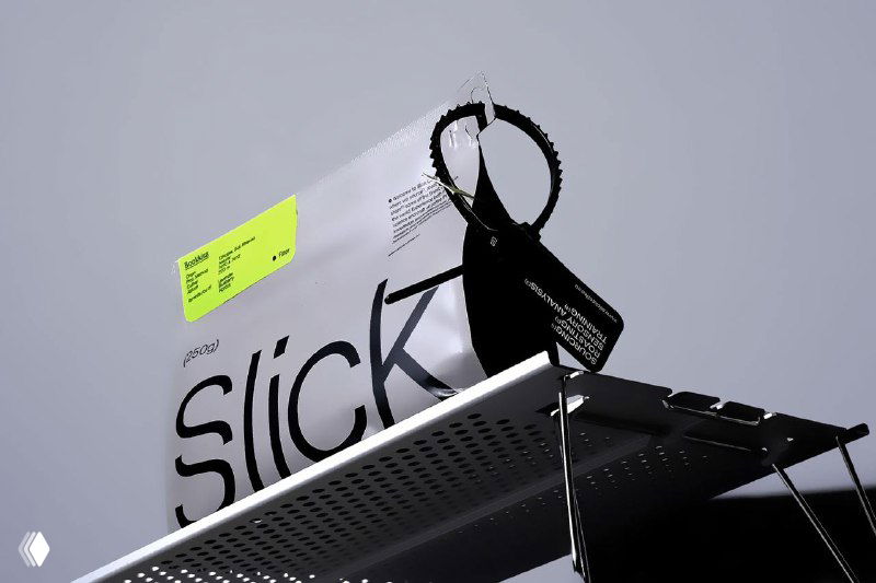 Пакет кофе Slick с яркой кислотной наклейкой и подвесом на металлической конструкции, контраст между матовым чёрным и неоном.