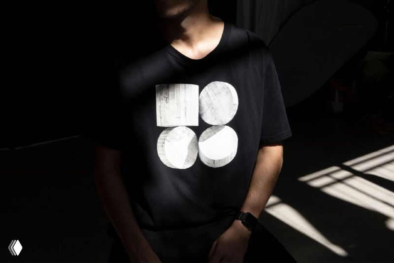 Человек в темной футболке с крупным белым графическим знаком из кругов — применение фирменного знака на одежде.