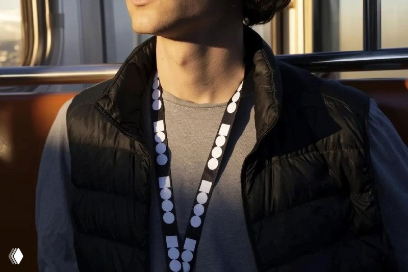 Крупный план бейджа и ланьярда с рядом белых круглых элементов — носимый элемент айдентики на человеке.