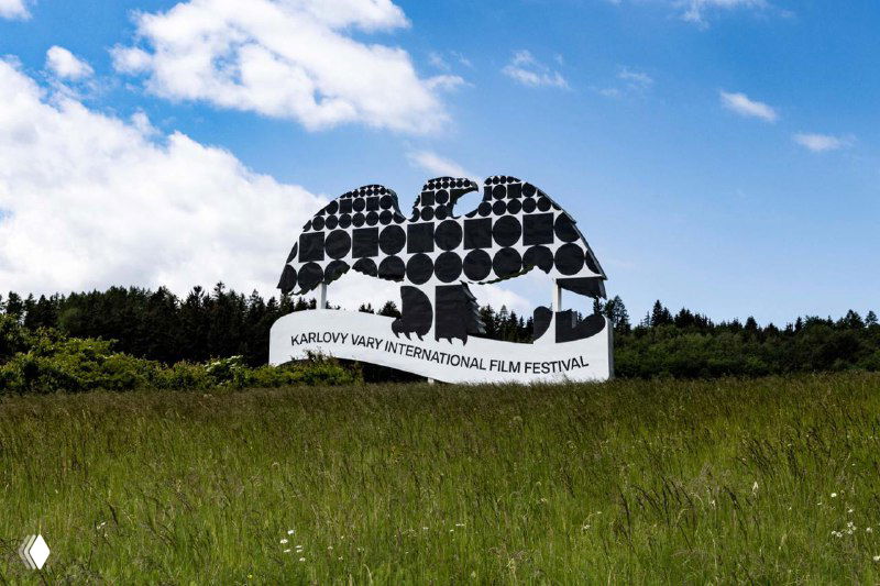 Наружная инсталляция в поле — скульптура или крупный баннер, составленный из множества черных круглых модулей на фоне природы.