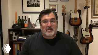 Кадр интервью: Андрей Герасимчук в домашней студии на фоне гитар, полок с книгами и предметов декора, крупный план