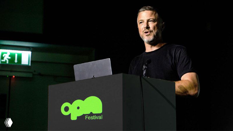 Докладчик за трибуной с эмблемой OPN на передней панели — пример применения айдентики в оформлении сцены и презентаций фестиваля.