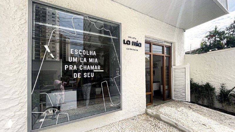 Фасад бразильского кафе La Mia: белая витрина с логотипом и стеклянной дверью, демонстрация фирменного оформления и входной зоны.