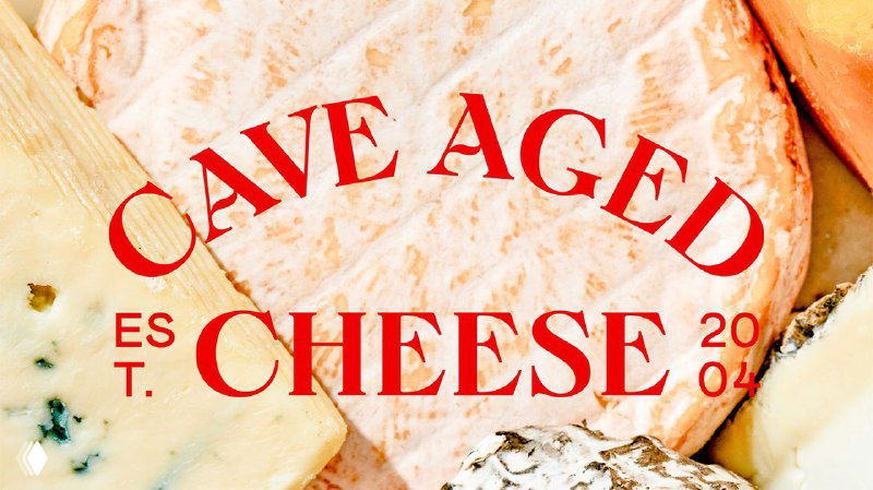 Крупный план круглого сыра с текстом «CAVE AGED CHEESE» красными буквами; видны корка, ломтики и текстура выдержанного сыра в фирменной палитре.