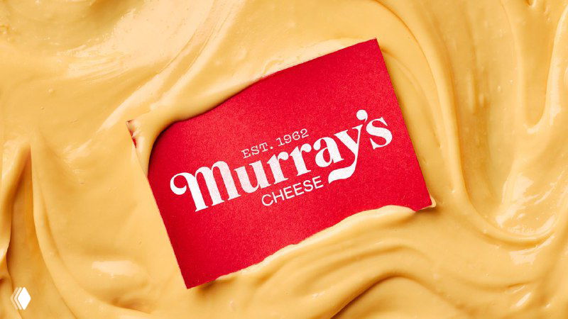 Красная фирменная карточка Murray’s расположена на кремовой текстуре сыра; крупный план логотипа и упаковочной эстетики бренда в применении.
