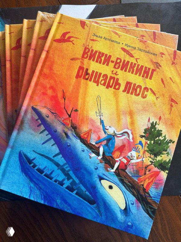 Стопка печатных экземпляров книги «Вики-Викинг и рыцарь Люс» с яркой обложкой: морской кит и герои в контрастных цветах, крупный план обложки.