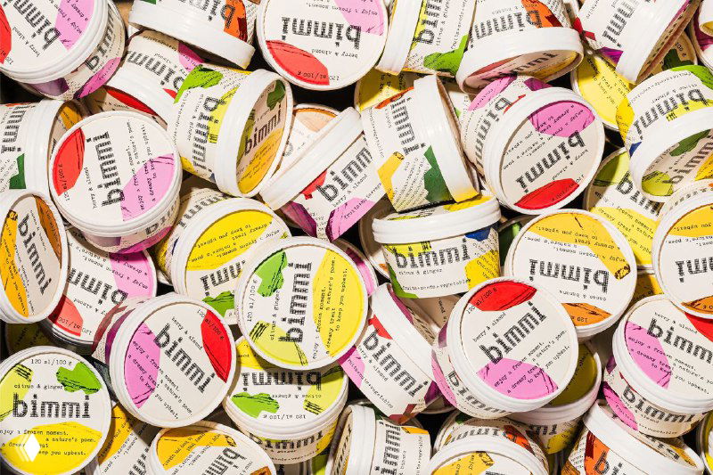 Крупный план множества круглых стаканчиков Bimmi с яркими бумажными этикетками, разнообразие цветов и узоров, демонстрация фирменного аналогового дизайна упаковки.