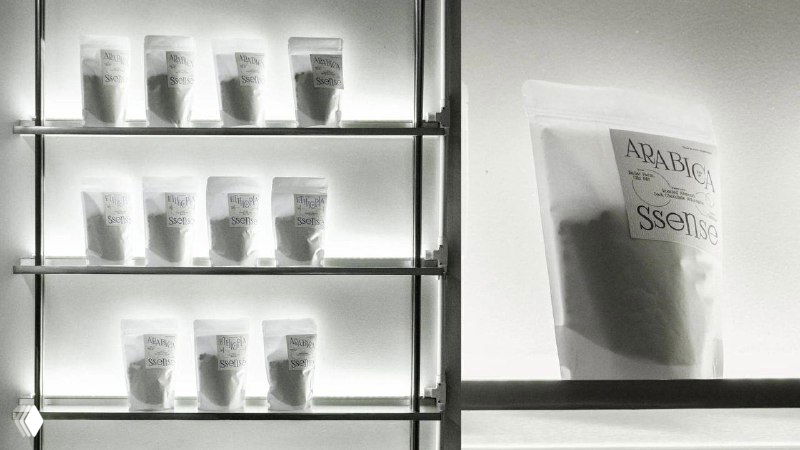 Черно‑белая фотография витрины с пакетиками кофе и стаканчиками на полках; минималистичная упаковка и акцент на текстуре бумаги и этикеток.