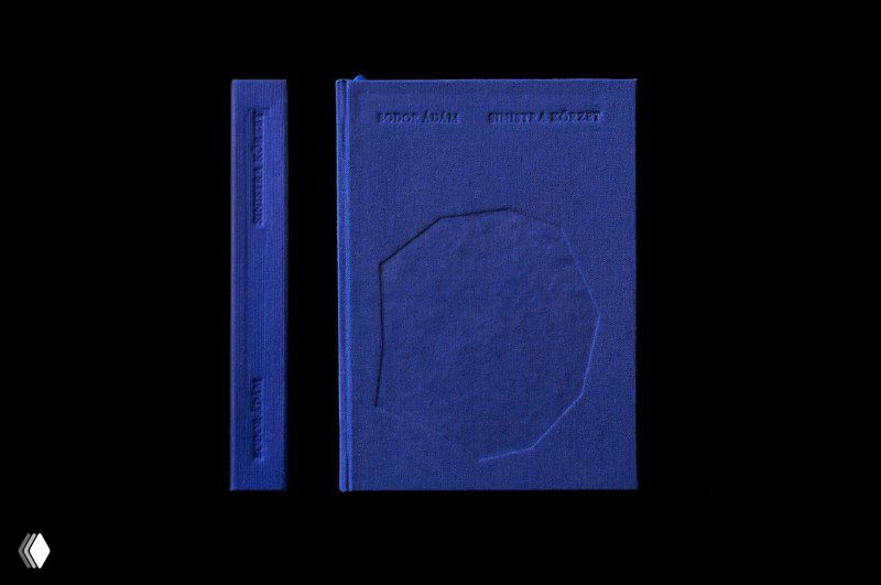 Синяя книжная обложка в однотонном дизайне на чёрном фоне: фронтальный вид, видна текстура переплёта и тиснёный элемент, минимализм оформления