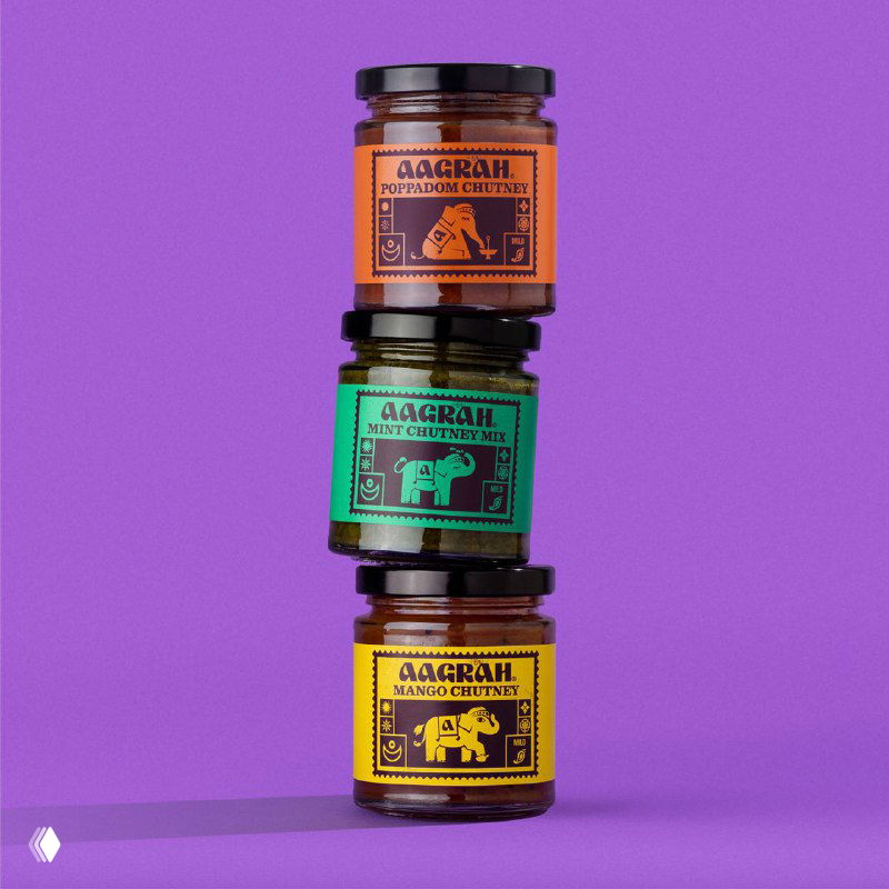 Три баночки соусов Aagrah, уложенные одна на другой на пурпурном фоне; яркие монохромные этикетки с декоративными слонами и орнаментами.