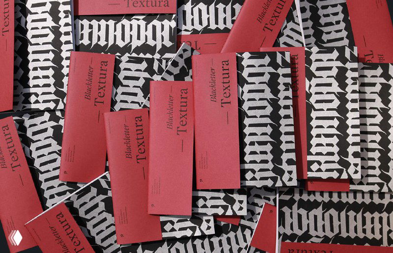 Разложенные экземпляры зина «Blackletter. Textura» с чёрно‑белой текстурой на обложках и красными вставками; общий вид композиции на столе.