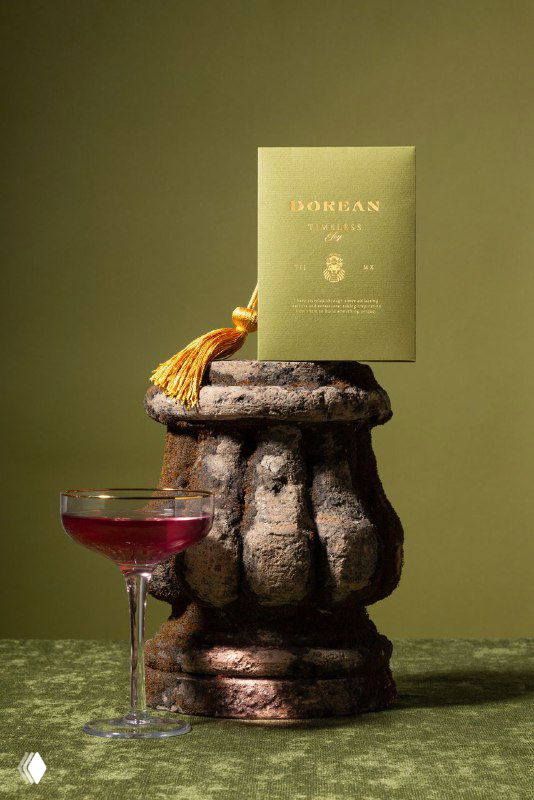 Зелёная визитка Dorean с золотой кисточкой, установленная на каменном постаменте рядом с коктейлем — предметная фотосъёмка элементa фирменного стиля.