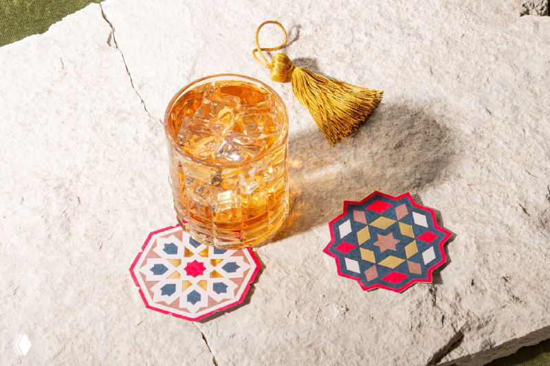 Крупный план коктейля на фактурной каменной плите рядом с орнаментальной подставкой и золотой кисточкой — детали айдентики Dorean в персидской эстетике.