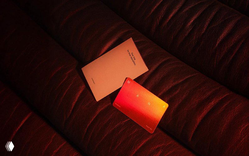 Макеты айдентики Mana, разложенные на тёмном диване: открытки и карточки, подсвеченные боковым тёплым светом, подчёркивающим минималистичный брендинг.