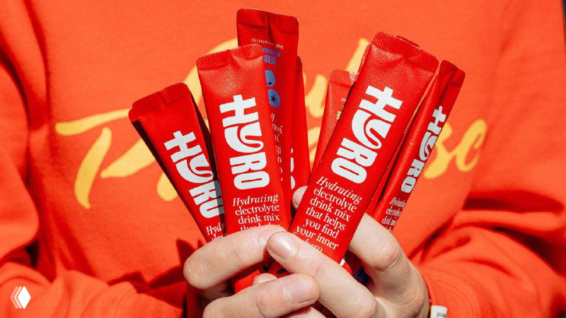 Руки держат несколько ярко‑красных саше Hyro на однотонном фоне; виден белый леттеринг‑логотип и фрагменты текста упаковки, акцент на бренде.