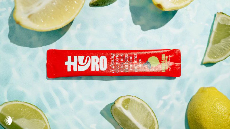 Горизонтально лежащее саше Hyro на фоне воды и ломтиков лимона; красная упаковка и белый логотип визуально выделяются на голубом фоне.