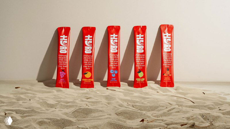 Несколько стоящих саше Hyro, установленных в песке; красные стик‑пакеты выстроены в ряд, видна унифицированная графика и фирменный шрифт бренда.