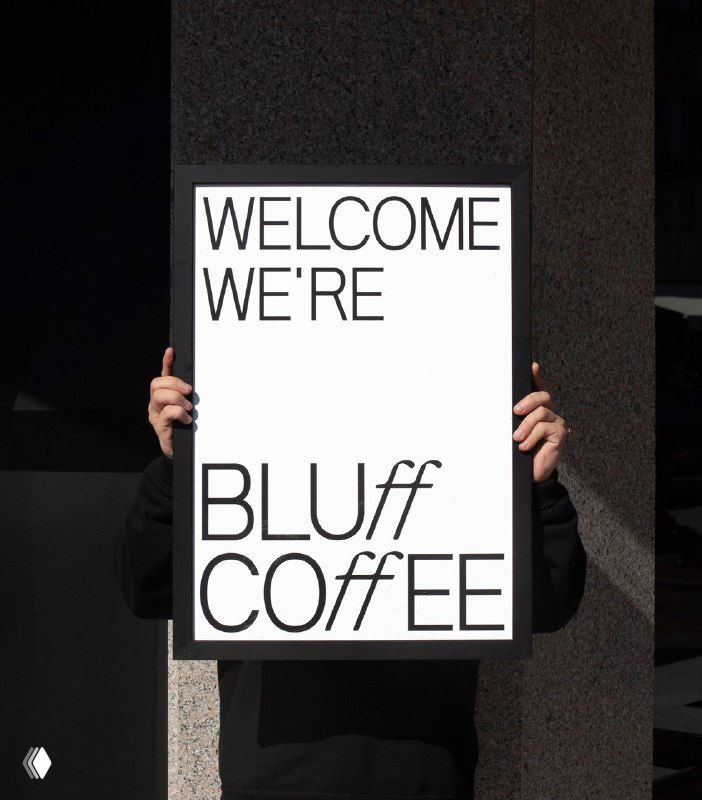 Человек держит рамку с плакатом «BLUff COFFEE» на белом поле — демонстрация логотипа и фирменной типографики кофейни в уличной сцене.