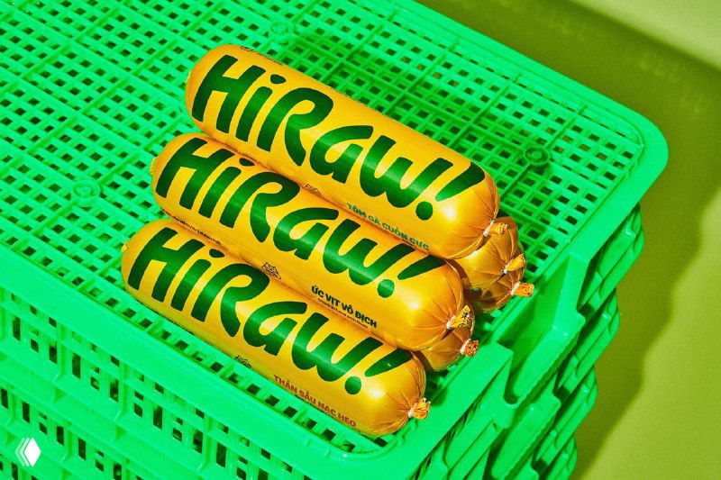 Ближайший план упаковок HiRaw, сложенных в пластиковый ящик; логотип хорошо читается, акцент на фактуре упаковки и цвете для ретейл-витрины.