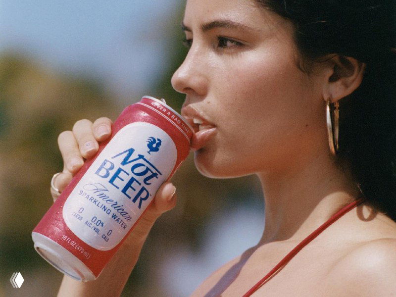 Модель делает глоток из банки «Not Beer» на улице; видно оформление банки, стилизацию под пиво и рекламный lifestyle‑образ продукта