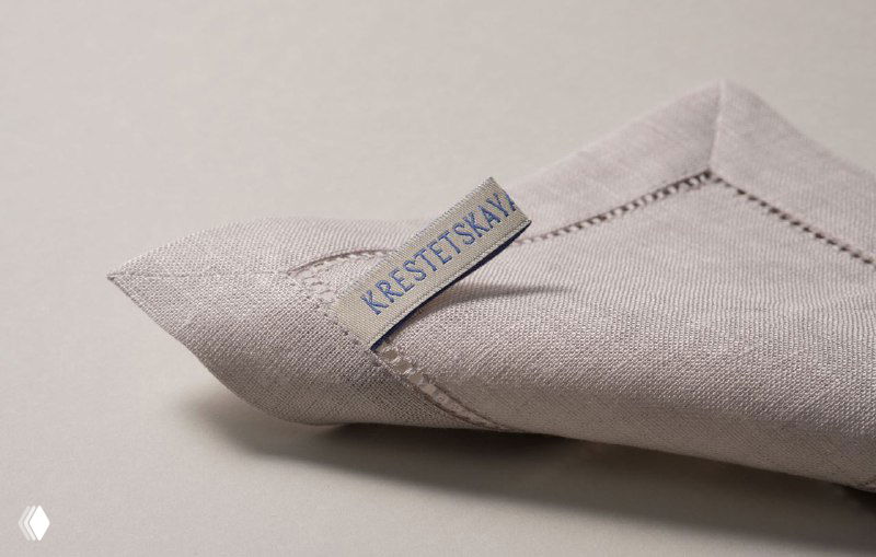 Тканевая бирка на натуральном льняном материале с синим текстом KRESTETSKAYA, демонстрация качества швов и фактуры ткани в ребрендинге.