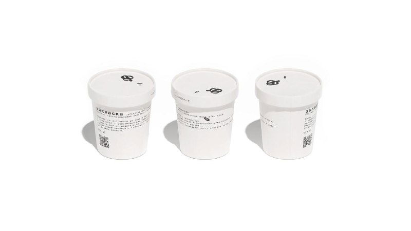 Три белых цилиндрических контейнера с минималистичной графикой и QR‑кодами на светлом фоне — часть фирменной упаковки Masa Madre.