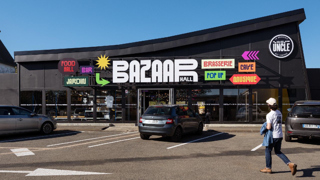 Фасад фудкорта с большой цветной вывеской «BAZAAR HALL», витрины, припаркованные машины и прохожий, иллюстрация айдентики в среде.