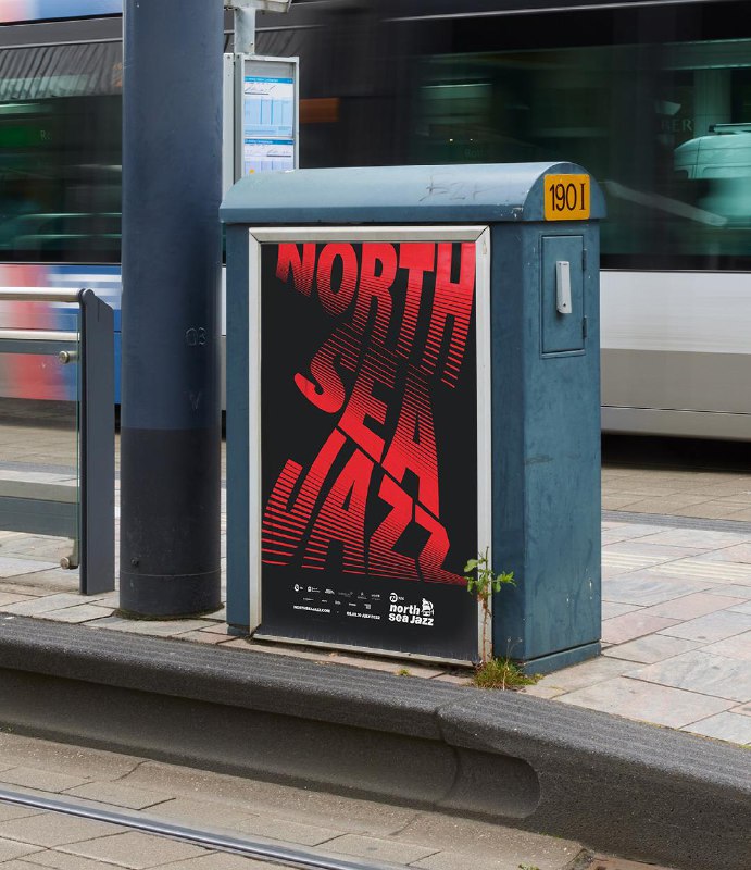 Уличный рекламный постер с искажённой вертикальной надписью «North Sea Jazz» на тёмном фоне, размещён у трамвайной остановки; городской рельсовый и урбанистический антураж виден.